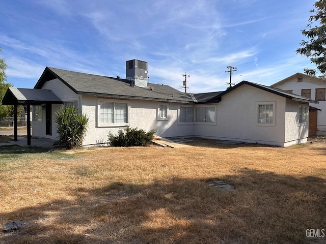 rear view of house with stucco siding, cooling unit, and a yard