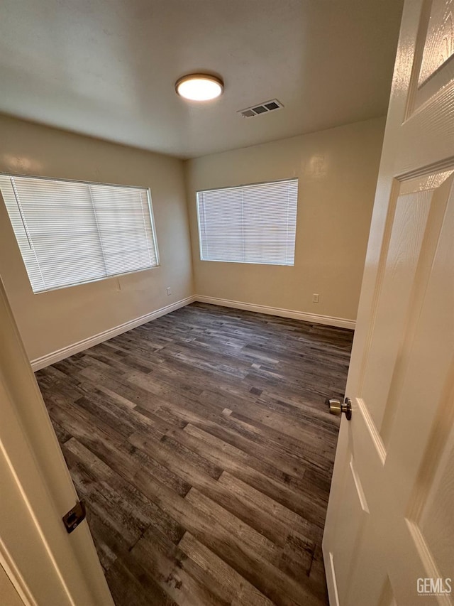 unfurnished room with dark wood-style flooring, visible vents, and baseboards