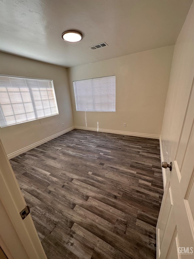 unfurnished room with dark wood-style flooring, visible vents, and baseboards