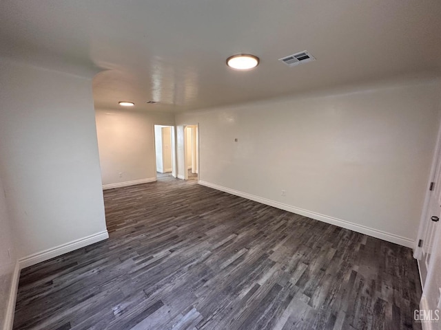 empty room with baseboards, visible vents, and dark wood-type flooring