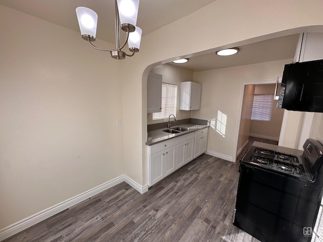 kitchen with dark wood-style floors, arched walkways, gas stove, white cabinetry, and a sink