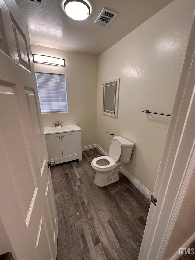 half bathroom featuring baseboards, visible vents, toilet, wood finished floors, and vanity