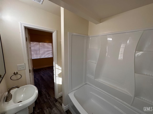 bathroom featuring a sink, bathing tub / shower combination, baseboards, and wood finished floors