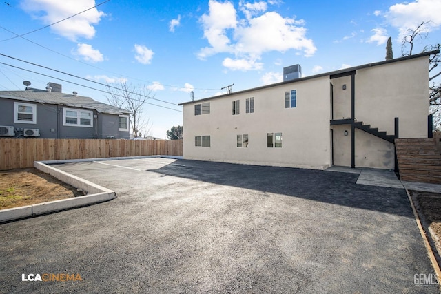 rear view of house with uncovered parking, fence, and stucco siding