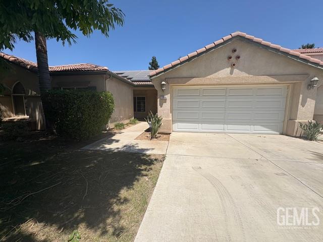 12006 Roaring River Ave, Bakersfield, CA 93311 - view of front facade featuring stucco siding, driveway, an attached garage, roof mounted solar panels, and a tiled roof