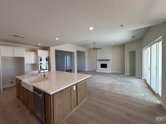 kitchen featuring stainless steel appliances, a sink, visible vents, white cabinetry, and a brick fireplace