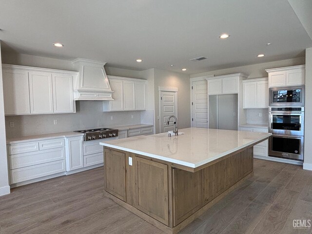 kitchen with dark wood finished floors, stainless steel appliances, visible vents, a sink, and premium range hood