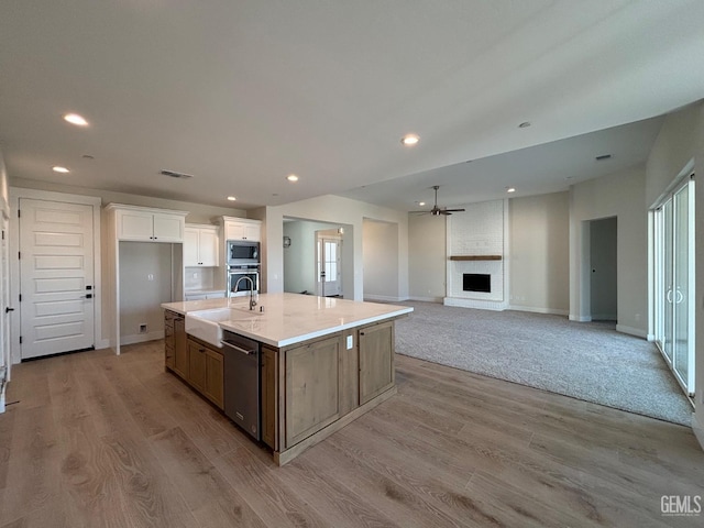 kitchen with visible vents, a brick fireplace, light wood-type flooring, a sink, and appliances with stainless steel finishes