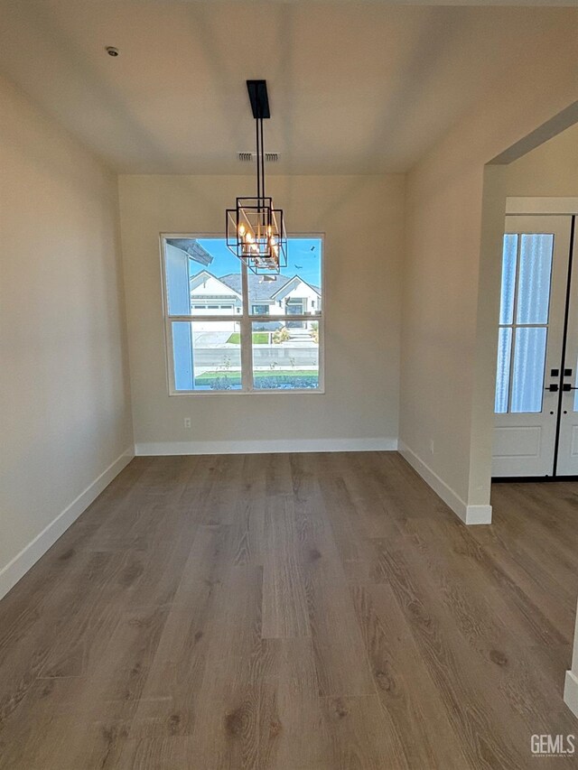 unfurnished dining area with a notable chandelier, visible vents, baseboards, and wood finished floors