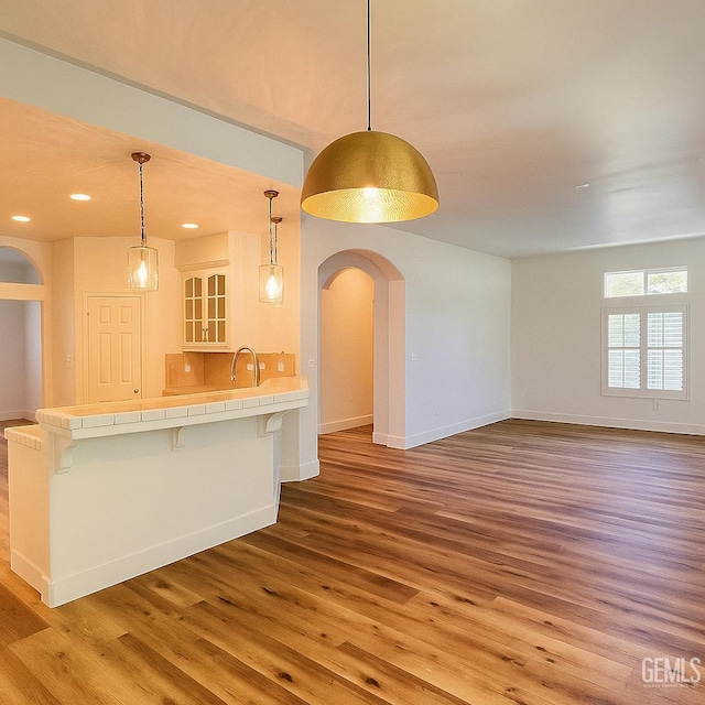 4812 Prairie Meadows Way, Bakersfield, CA 93312 - kitchen featuring tile counters, wood finished floors, a breakfast bar, arched walkways, and hanging light fixtures