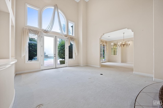 unfurnished living room with a notable chandelier, light carpet, and a high ceiling