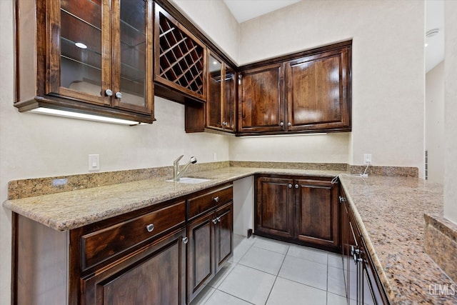 kitchen with dark brown cabinetry, light stone counters, sink, and light tile patterned floors