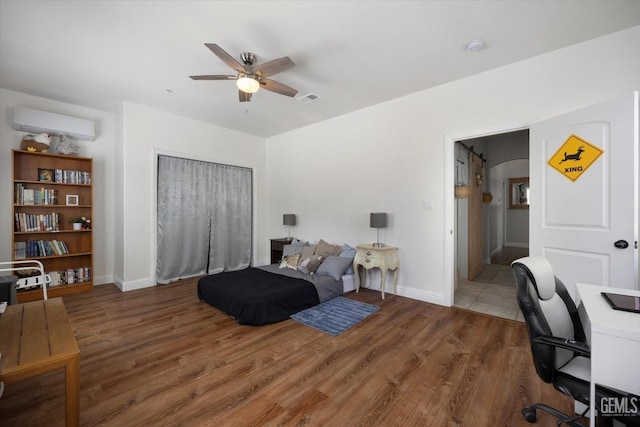 bedroom featuring wood-type flooring, a wall unit AC, and ceiling fan