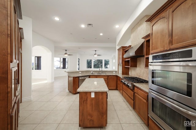 kitchen with sink, wall chimney exhaust hood, appliances with stainless steel finishes, a kitchen island, and kitchen peninsula