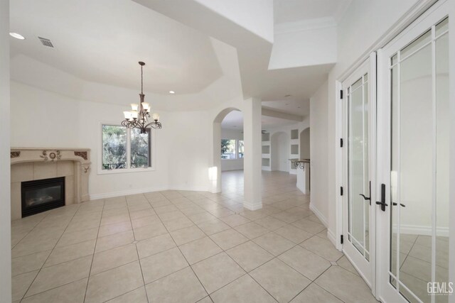 unfurnished living room featuring a tile fireplace, ornamental molding, a notable chandelier, and light tile patterned flooring