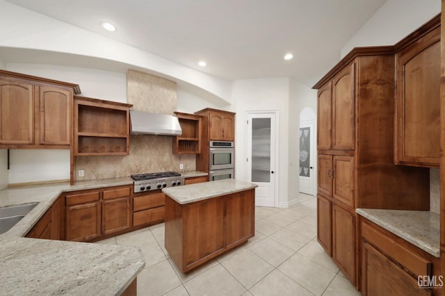 kitchen featuring wall chimney exhaust hood, light stone counters, light tile patterned floors, and appliances with stainless steel finishes