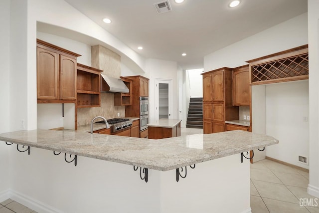 kitchen with a kitchen breakfast bar, wall chimney range hood, decorative backsplash, light stone counters, and kitchen peninsula