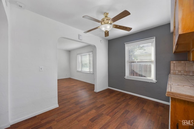 1909 Carrere St, Bakersfield, CA 93308 - unfurnished dining area with arched walkways, dark wood-style flooring, ceiling fan, and baseboards