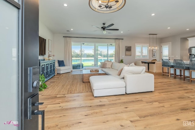 living room with ceiling fan with notable chandelier and light wood-type flooring