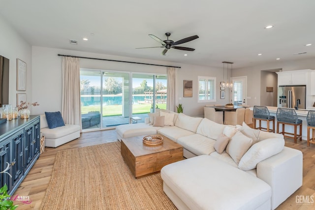 living room with ceiling fan with notable chandelier, a healthy amount of sunlight, and light hardwood / wood-style flooring