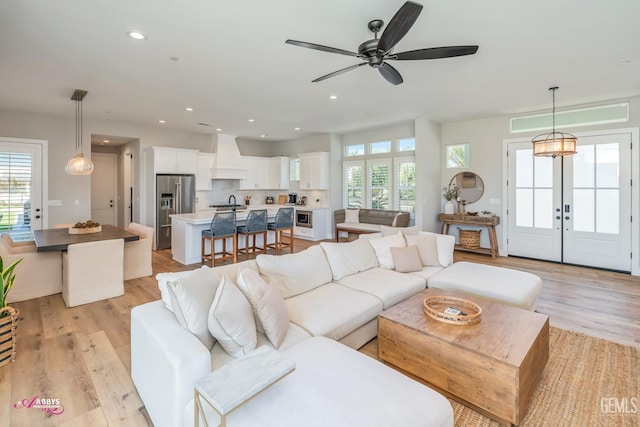 living room with ceiling fan with notable chandelier, light wood-type flooring, and french doors