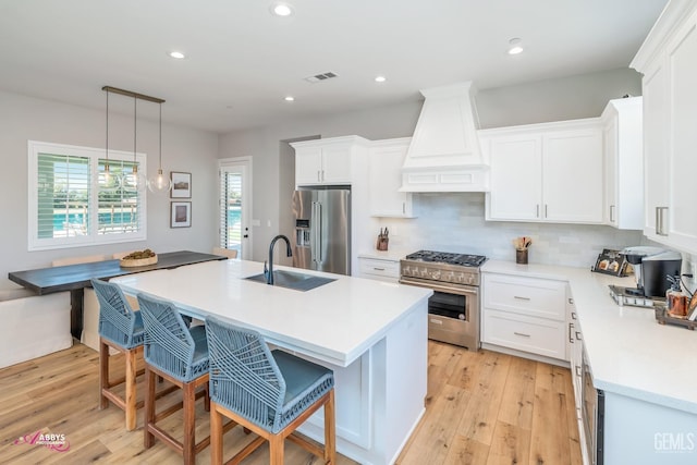 kitchen with custom exhaust hood, sink, decorative light fixtures, an island with sink, and premium appliances