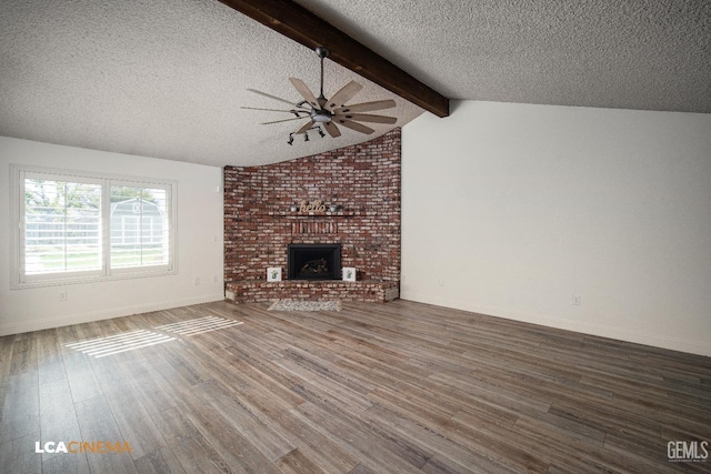 unfurnished living room with dark wood-type flooring, vaulted ceiling with beams, a textured ceiling, a brick fireplace, and ceiling fan