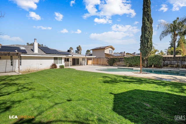 rear view of property with a yard, a fenced in pool, a patio area, and solar panels