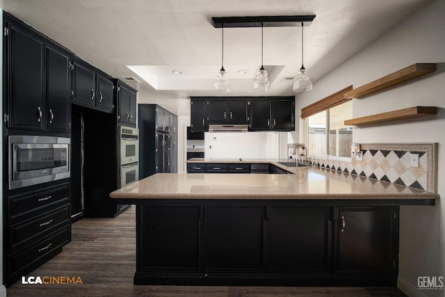 kitchen with kitchen peninsula, decorative light fixtures, a tray ceiling, stainless steel appliances, and light stone countertops