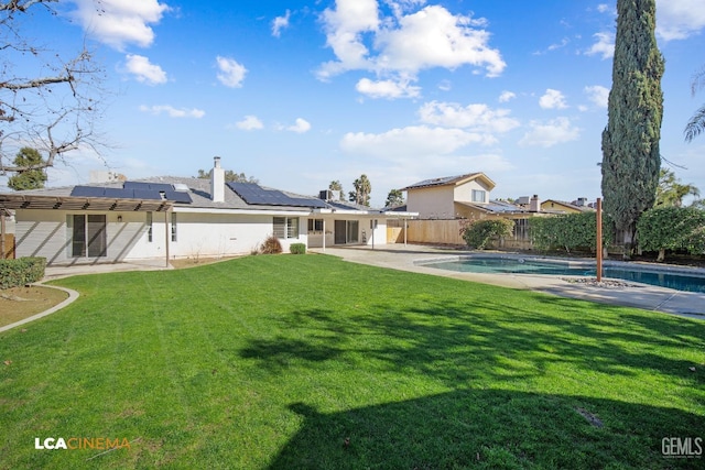 rear view of house featuring a fenced in pool, a lawn, a patio, and solar panels