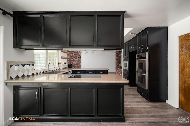 kitchen with sink, kitchen peninsula, hardwood / wood-style flooring, stainless steel appliances, and backsplash