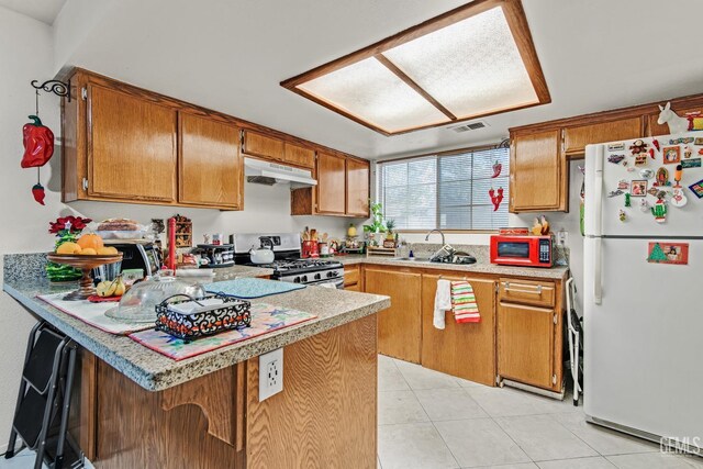 kitchen with stainless steel gas range oven, white refrigerator, sink, kitchen peninsula, and a breakfast bar area