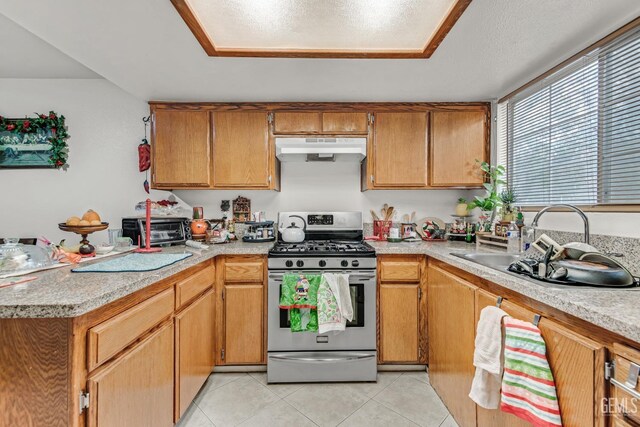 kitchen featuring kitchen peninsula, light tile patterned floors, stainless steel gas range oven, and sink