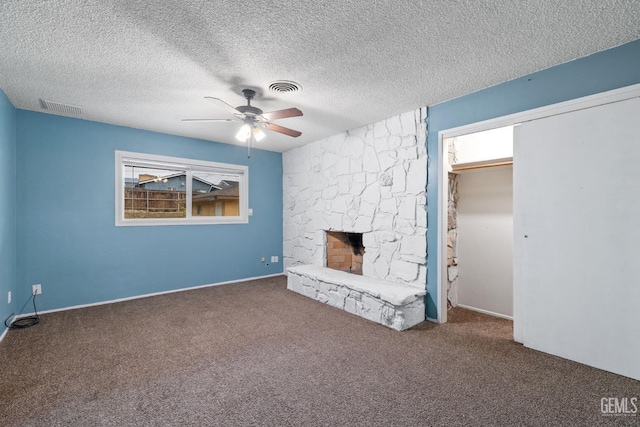 unfurnished living room with ceiling fan, a fireplace, a textured ceiling, and dark colored carpet