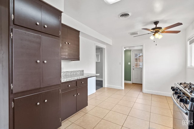 kitchen featuring stainless steel range with gas cooktop, ceiling fan, light stone countertops, light tile patterned floors, and dark brown cabinetry