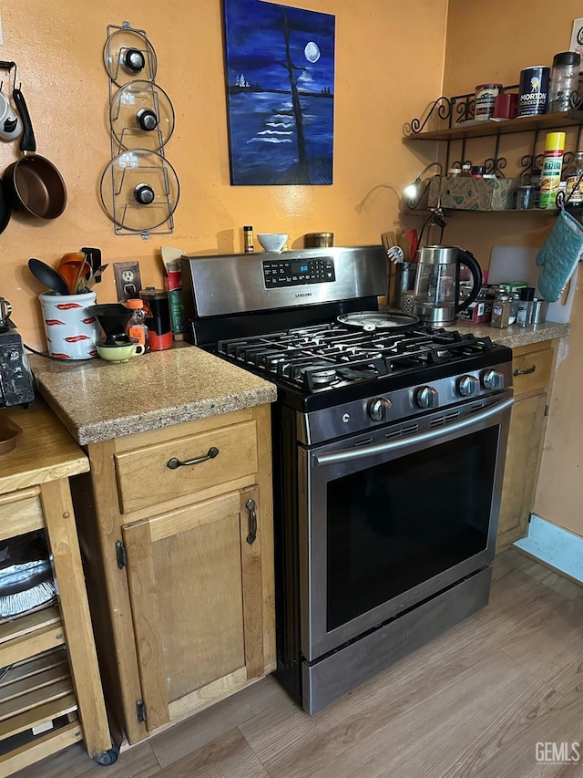 kitchen with light brown cabinets, light wood-type flooring, stainless steel range with gas cooktop, and light stone counters