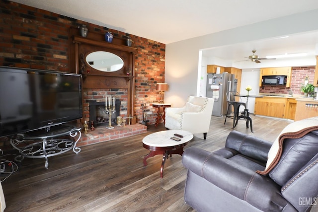 living room with a ceiling fan, a brick fireplace, and wood finished floors