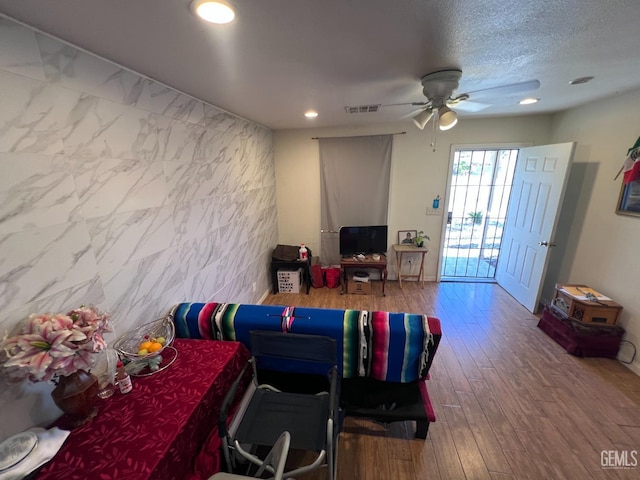 living room with hardwood / wood-style flooring, ceiling fan, tile walls, and a textured ceiling