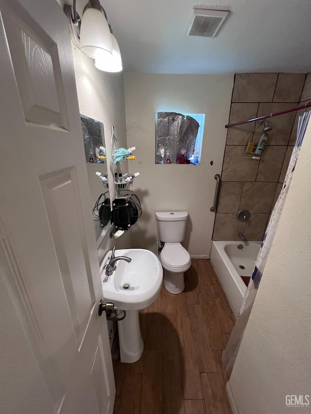 full bathroom with tiled shower / bath combo, toilet, wood-type flooring, and sink