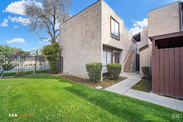 view of front facade with stucco siding, fence, a front lawn, and stairs