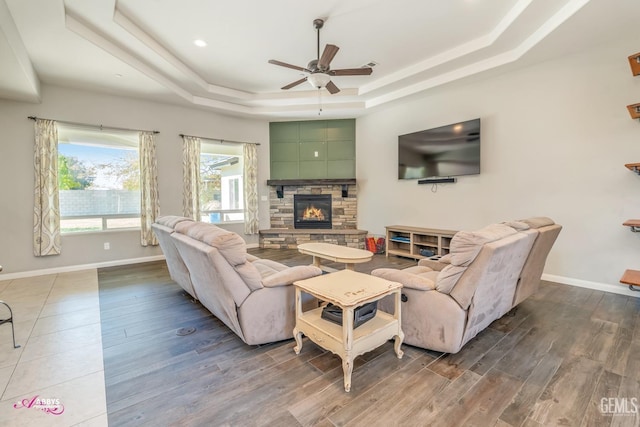 living room featuring hardwood / wood-style floors, ceiling fan, a fireplace, and a tray ceiling