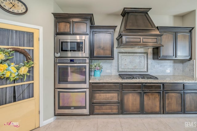 kitchen with custom range hood, stainless steel appliances, light stone counters, and tasteful backsplash