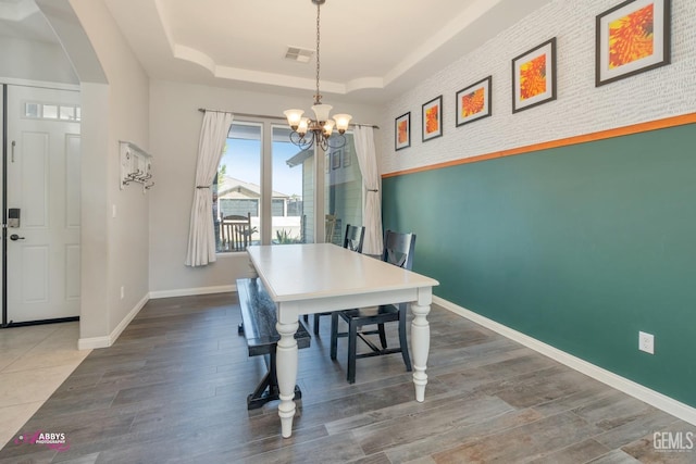 dining room featuring a tray ceiling, brick wall, and an inviting chandelier