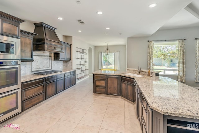 kitchen featuring backsplash, a large island, light stone counters, custom range hood, and stainless steel appliances