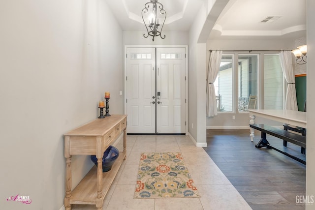 entryway with a raised ceiling, light tile patterned flooring, and a chandelier