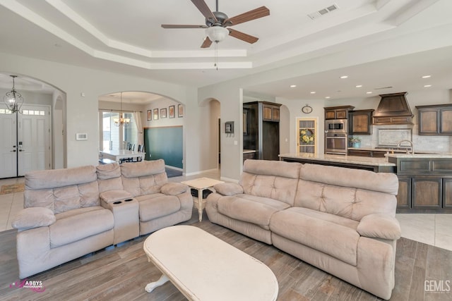 living room featuring ceiling fan with notable chandelier and a tray ceiling