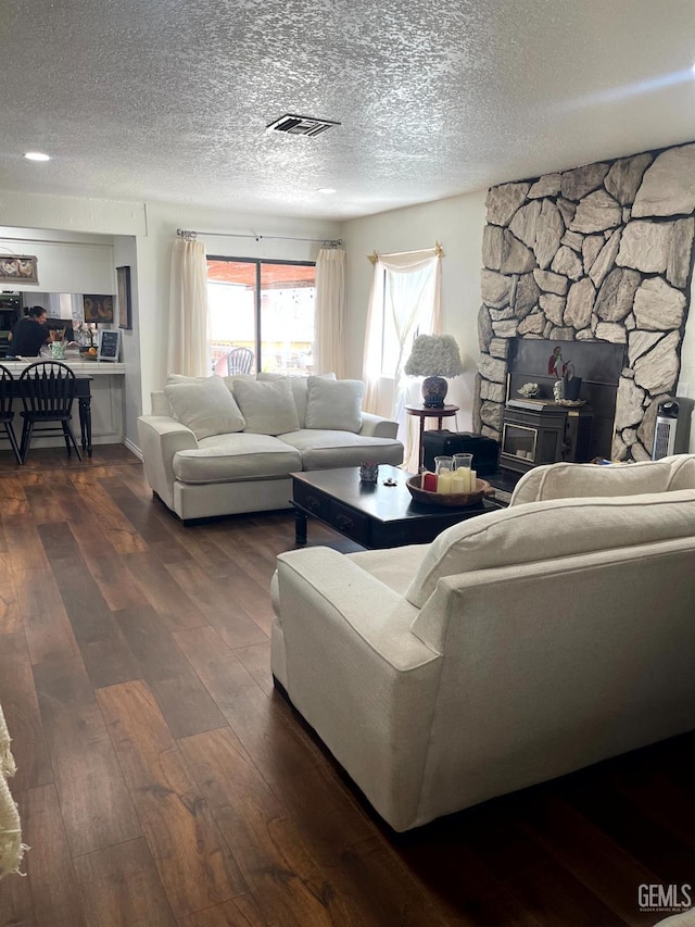living area featuring visible vents, a textured ceiling, dark wood finished floors, and a wood stove
