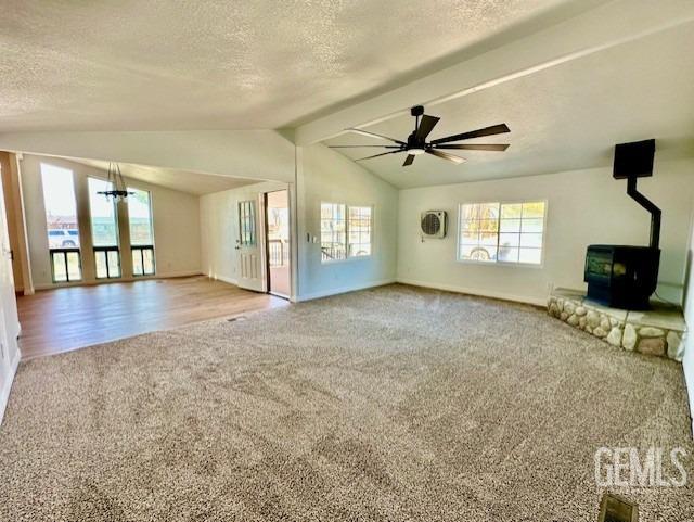 unfurnished living room with vaulted ceiling with beams, carpet floors, a textured ceiling, and a wood stove