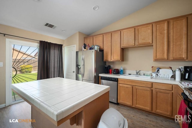 kitchen with a sink, vaulted ceiling, tile countertops, and stainless steel appliances