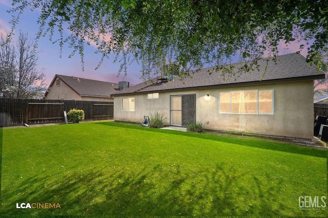 back of property at dusk featuring central air condition unit, a lawn, a fenced backyard, and stucco siding